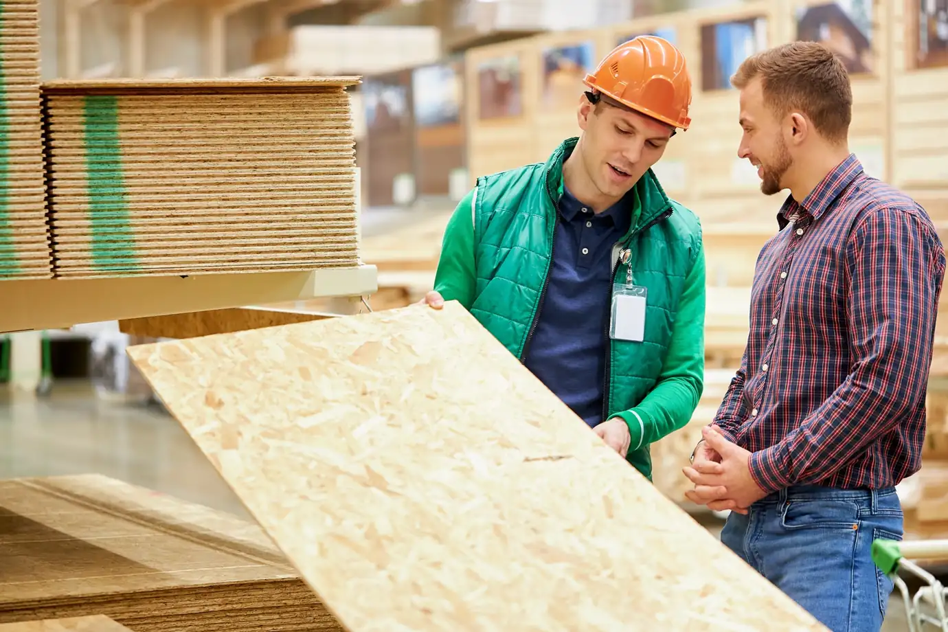 Worker in high-vis vest showing OSB plywood boards to a customer at a merchant floor